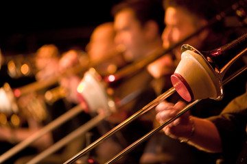 Jazz Big Band trombone section with cup mutes. Shallow focus on the foreground trombonist with the rest of the section falling into background blur.