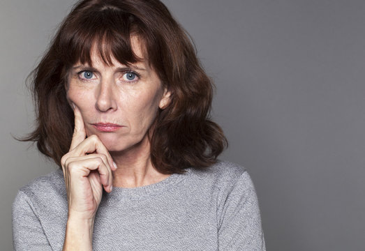 displeased mature woman with brown hair and grey sweater thinking,face leaning on finger,looking straight angry and stressed out