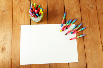 Colorful pastel crayons with white sheet of paper on wooden background