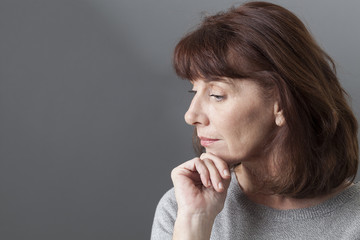 thinking mature woman with brown hair and grey sweater on profile,looking serene or with SAD syndrome,copy space