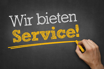 Hand schreibt Text "Wir bieten Service!" auf Kreidetafel