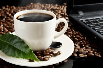 Cup of coffee with mist,laptop,coffee leaf at breakfast