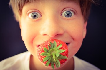 Wide eyed child with a fresh strawberry in his mouth