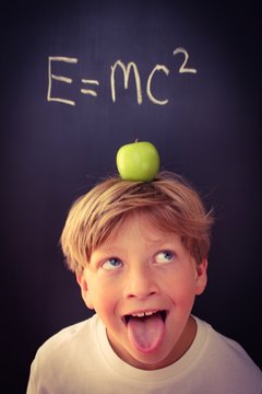 Child with his tongue sticking out balancing an apple on his head next to a formula