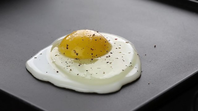 Cooking fried eggs on electric barbecue, salting and papering
