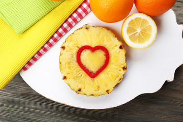 Pineapple slice with cut in shape of heart and different fruits on table close up