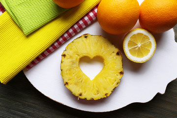 Pineapple slice with cut in shape of heart and different fruits on table close up