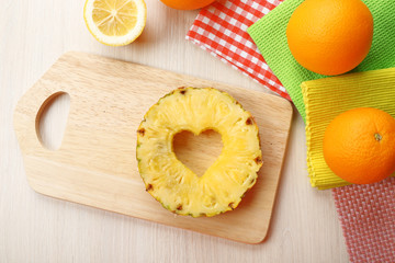Pineapple slice with cut in shape of heart and different fruits on table close up