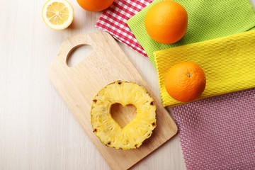 Pineapple slice with cut in shape of heart and different fruits on table close up