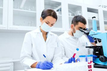 scientists with clipboard and microscope in lab