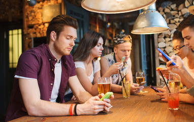 friends with smartphones and drinks at bar