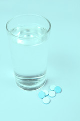 A glass of water and Pills, medicals, drugs, tablets in white