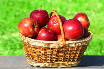 Ripe red apples in wicker basket outdoors