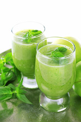 Glasses of green healthy juice with basil and apples on metal tray close up