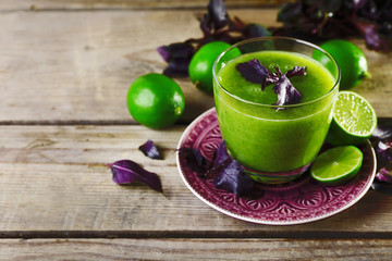 Glass of green healthy juice with basil and limes on table close up