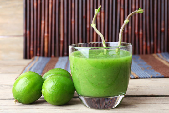 Glass of green healthy juice with limes on wooden background