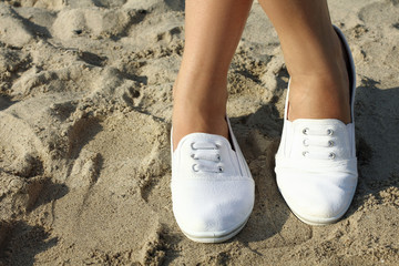 Girl`s legs in white shoes on the sand