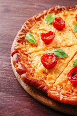 Slices of tasty cheese pizza with basil and cherry tomatoes on table close up