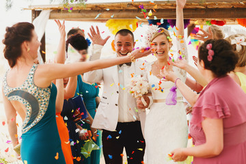 Naklejka premium beautiful gorgeous blonde bride and stylish groom under confetti, hawai colorful sand ceremony on cyprus
