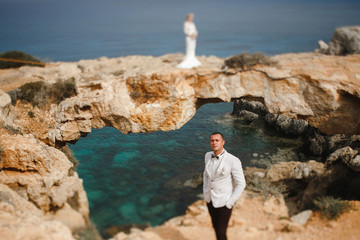 Fototapeta na wymiar beautiful gorgeous blonde bride and stylish groom on rocks, on the background of a sea, wedding ceremony on cyprus