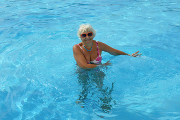 Fototapeta na wymiar Aged woman is standing in bright blue pool water.