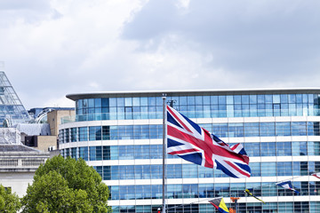 Fototapeta premium Waving in the wind British union flag in front of a glass window modern office building in London