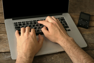 Man working on laptop on wooden table close up