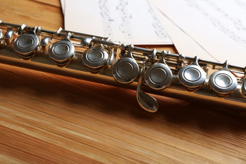 Obraz premium Silver flute with music notes on wooden table close up