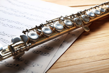 Obraz premium Silver flute with music notes on wooden table close up