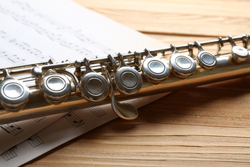 Obraz premium Silver flute with music notes on wooden table close up
