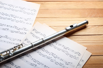 Fototapeta premium Silver flute with music notes on wooden table close up