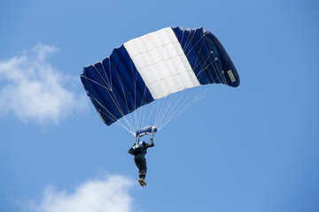 Parachutist on a striped blue white parachute on bakcground blue sky with clouds