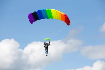 Afwasbaar Fotobehang Luchtsport Parachutist op een heldere parachute regenboogkleuren op bakcground blauwe lucht met wolken