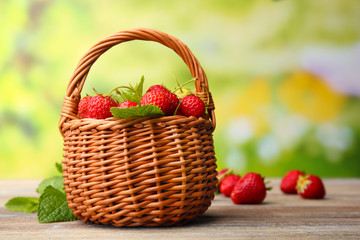 Fototapeta na wymiar Ripe strawberries in wicker basket on wooden table on blurred background