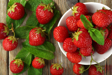 Ripe strawberries in saucer on wooden table, top view