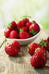Ripe strawberries in saucer on wooden table on blurred background