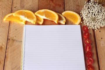Diary book with orange and tomatoes slice on wooden background.