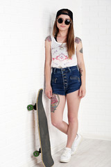 Beautiful hipster girl with skateboard on light background