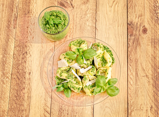Top view of a glass plate of basil ricotta tortelloni with pesto and parmesan flakes.