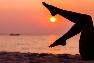 Female legs silhouette on sunset sea background, side view, back lit