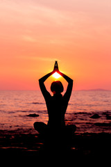 Woman silhouette sitting in lotus position on sunset sea background back lit