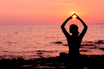 Woman silhouette sitting in lotus position on sunset sea background back lit