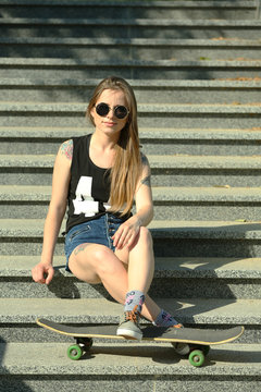 Beautiful tattooed girl with skateboard  on stairs, outdoors