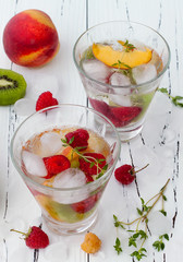 Healthy detox fruit infused flavored water. Summer refreshing homemade cocktail with fruits and thyme on white wooden table