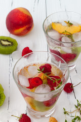 Healthy detox fruit infused flavored water. Summer refreshing homemade cocktail with fruits and thyme on white wooden table