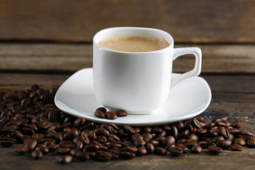 Cup of coffee and beans on wooden table close up