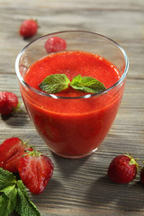 Glass of strawberry smoothie with berries on wooden table close up