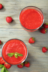 Glasses of strawberry smoothie with berries on wooden table close up