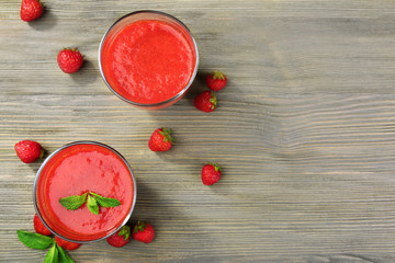 Glasses of strawberry smoothie with berries on wooden table close up