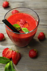 Glass of strawberry smoothie with berries on wooden table close up